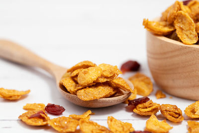The wooden bowl of caramel cornflakes with raisins on white background