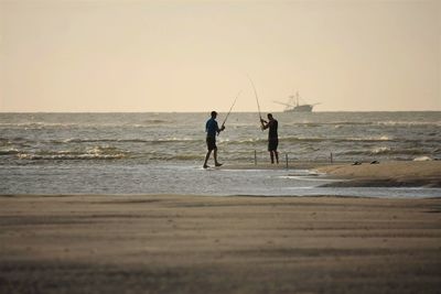 Silhouette men fishing on shore against clear sky during sunset