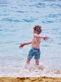 Full length of boy splashing water in sea