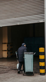 Rear view of man pulling garbage bin