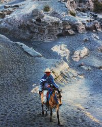 Rear view of man riding hores on rock mt. bromo