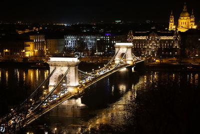 Illuminated bridge over river with city in background at night