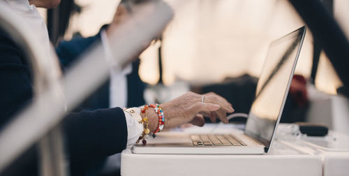 Cropped image of senior woman using laptop with senior man in background at yacht