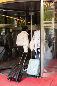 Young female tourists with wheeled luggage entering through revolving door at hotel