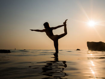 Silhouette woman practicing yoga in sea during sunset