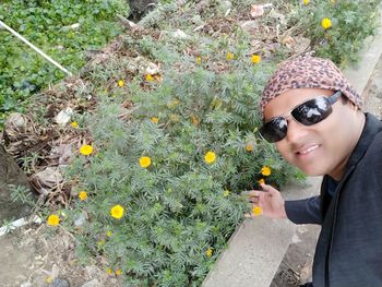 Portrait of young woman holding sunglasses on red flowering plants