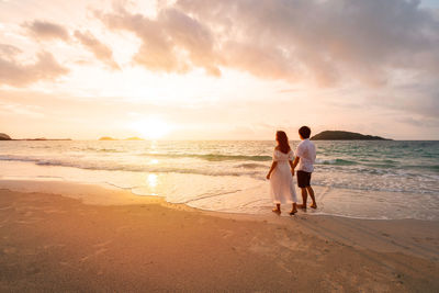 Rear view of women on beach against sky during sunset