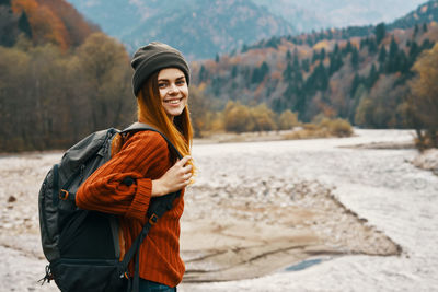 Portrait of smiling young woman standing against mountains