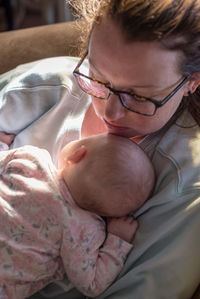 High angle view of mother sitting with toddler daughter on sofa