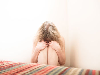 Sad woman sitting against wall at home