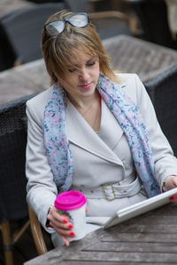 Young holding drink while using digital tablet on table