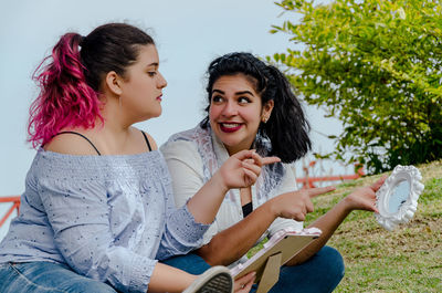 Friends holding mirror frame while sitting at park