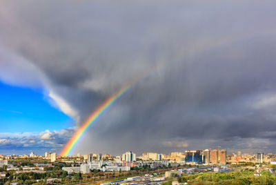 A bright rainbow in the sky above city houses after a thunderstorm separates thunderclouds