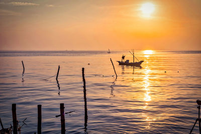 Silhouette people on sea against sky during sunset