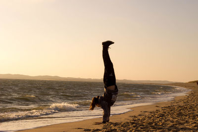 Teenage girl doing handstand on shore at beach during sunset