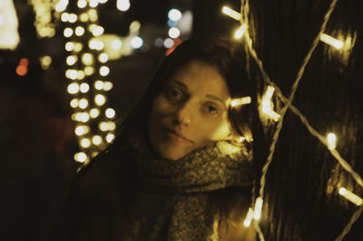 Portrait of young woman looking at illuminated christmas lights at night