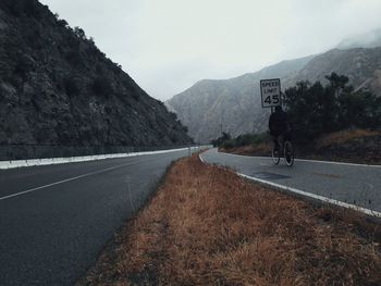 Man riding bicycle on road by mountain against sky