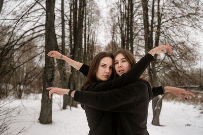 Portrait of female friends embracing in forest during winter