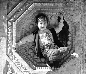 Portrait of boy crouching in carvings on wall