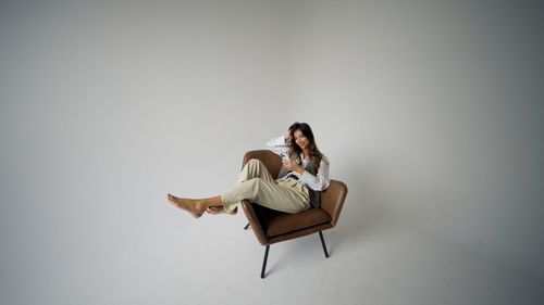 Young woman sitting on chair against wall