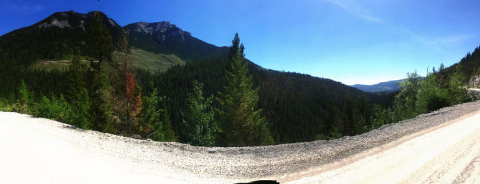 Panoramic shot of road by mountains against blue sky