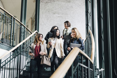Low angle view of smiling female entrepreneurs moving down on staircase in office
