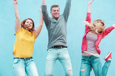 Young friends with arms raised jumping against wall