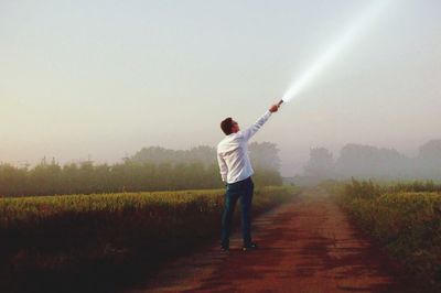 Rear view of man standing on field against sky