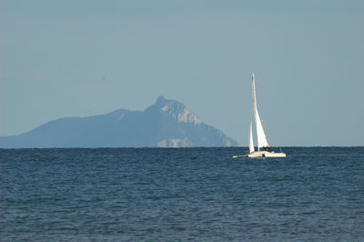 Distant view of sailboat sailing in sea against clear sky