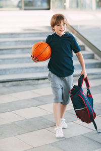 A cute boy with a backpack in one hand and a basketball in the other. 