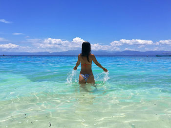 Rear view of woman wearing bikini standing in sea against sky