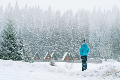 Man in worm clothing looking at wooden cabins during blizzard