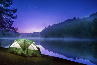 Tent by lake against sky at night