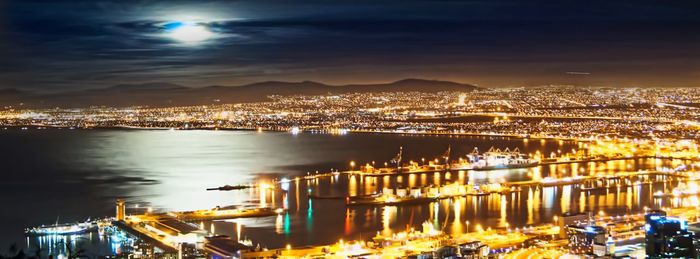 Illuminated city by river against sky at night