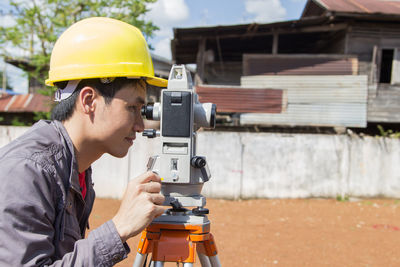 Side view of engineer looking through theodolite at construction site