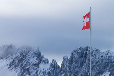 Low angle view of swiss flag against snowcapped mountain