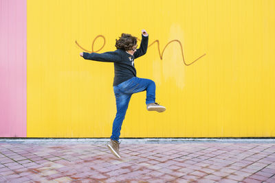 Side view of teenage boy jumping against yellow wall