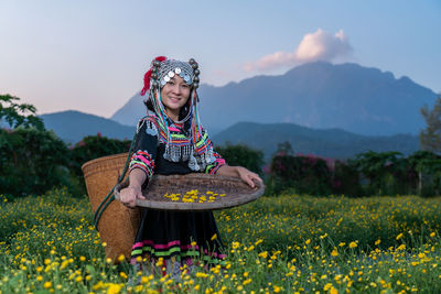 Portrait of smiling woman in traditional clothing holding wicker basket while standing in farm