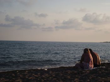 People sitting on beach looking at sea against sky