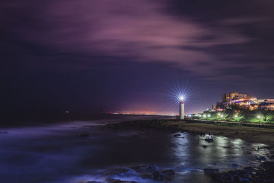 Illuminated city by sea against sky at night