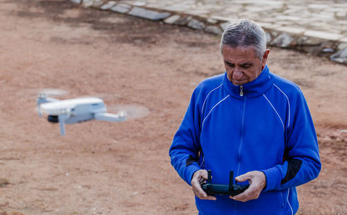 Side view of man flying the drone looking at the remote control while standing against the trees in the park