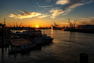 Cranes at harbor against sky during sunset