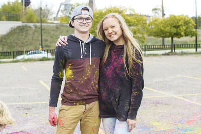 Portrait of happy friends with powder paint standing on footpath at park