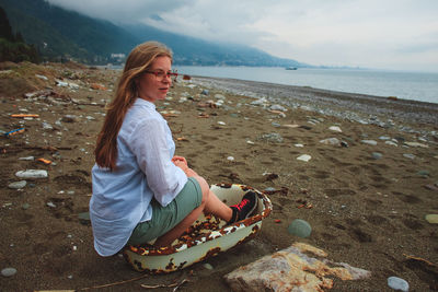 Woman sitting on abandoned bathtub at sandy beach