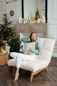 Young happy woman holds a pillow in her hands while sitting in a cozy armchair in the living room