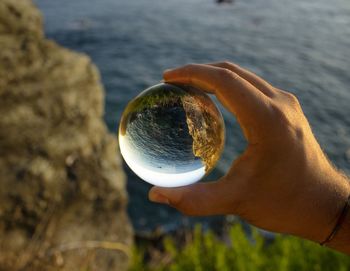 Cropped hand of man holding crystal ball against sea