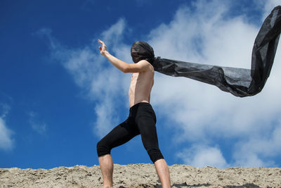 Shirtless man with scarf standing against sky