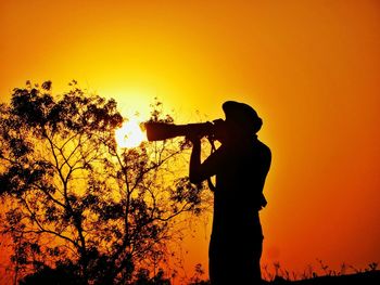 Silhouette man standing by tree against orange sky