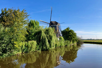 Traditional windmill by lake against sky