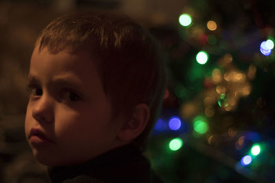 Close-up portrait of cute boy against  illuminated christmas tree